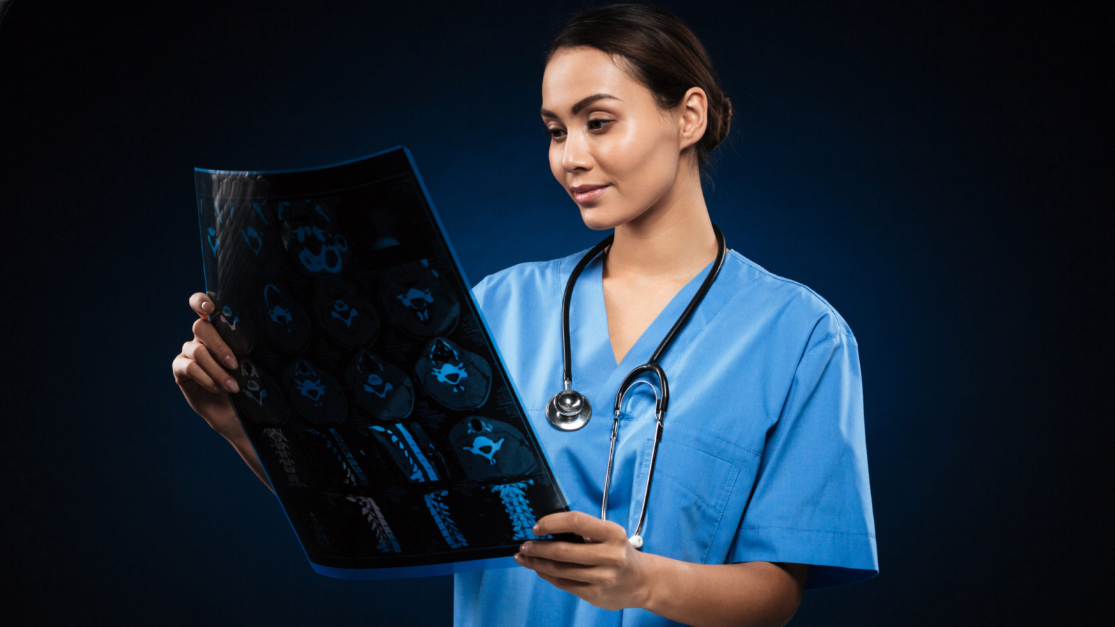 Young concentrated lady doctor with stethoscope looking at x-ray image isolated