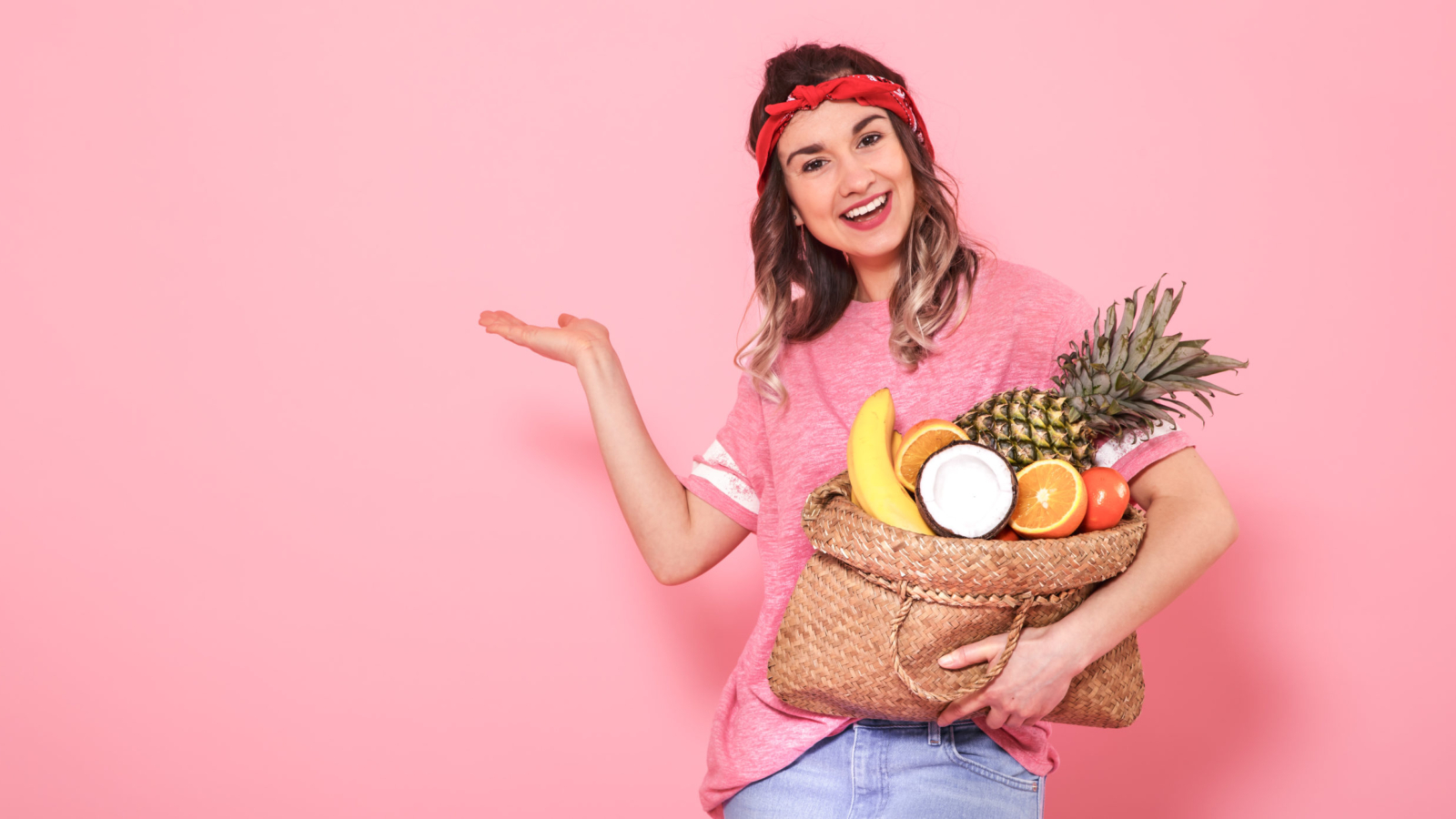 Horizontal portrait of hipster girl in stylish clothing, with bag with fruit, on pink background, lifestyle concept